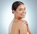 Portrait of beautiful woman with smooth glowing skin and copyspace posing topless and touching shoulder. Smiling caucasian model isolated against a grey studio background with healthy skincare routine