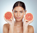 Closeup portrait of beautiful woman holding grapefruit while posing topless. Caucasian model isolated against a grey background in a studio with smooth glowing skin, fresh healthy skincare routine