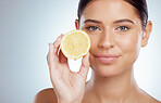 Closeup portrait of beautiful woman holding ripe lemon while posing topless. Caucasian model isolated against a grey background in a studio with smooth glowing skin, fresh healthy skincare routine
