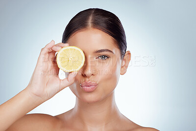 Portrait of pouting woman holding ripe lemon over her eye while posing topless with copyspace. Caucasian model isolated against grey studio background with smooth skin, fresh healthy skincare routine