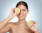 Portrait of smiling woman holding ripe lemon over her eye while posing topless with copyspace. Caucasian model isolated against grey studio background with smooth skin, fresh healthy skincare routine