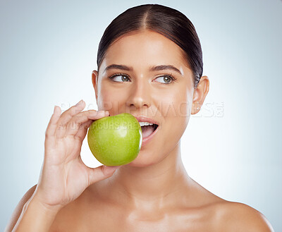 Beautiful woman biting into a green apple while posing with copypsace. Caucasian model looking contemplative while isolated against a grey studio background. Eating healthy is part of skincare routine