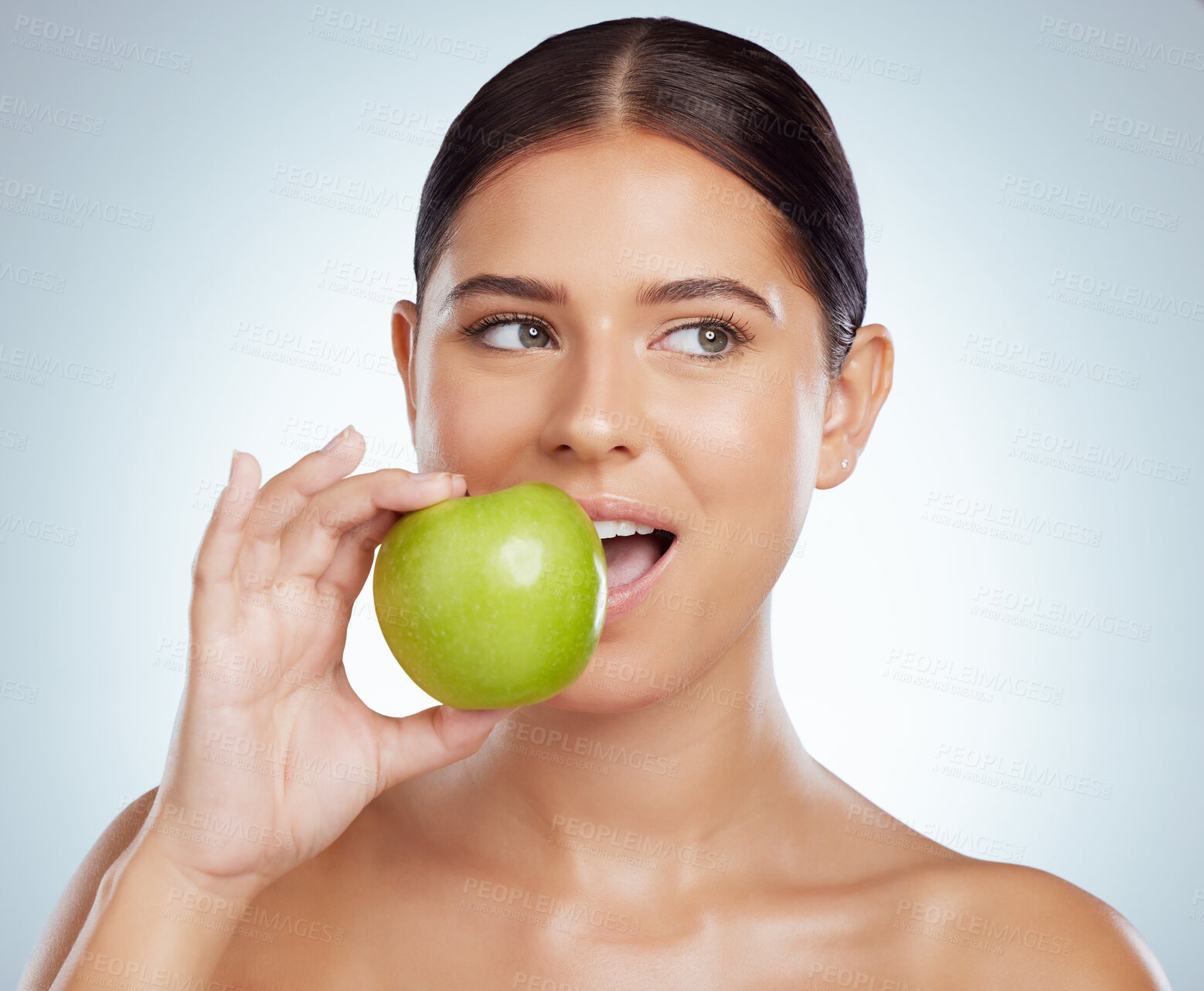 Buy stock photo Beautiful woman biting into a green apple while posing with copypsace. Caucasian model looking contemplative while isolated against a grey studio background. Eating healthy is part of skincare routine