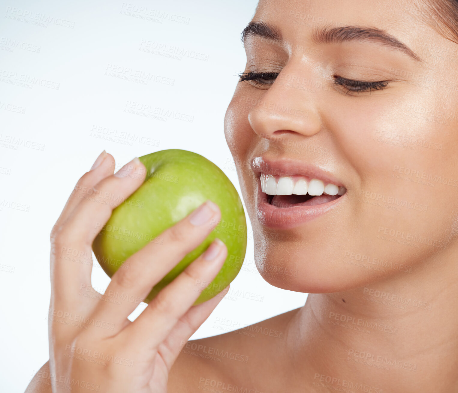 Buy stock photo Closeup of smiling beautiful woman biting into a green apple while posing. Happy caucasian model isolated against a grey background in a studio. Eating healthy is part of a good skincare routine