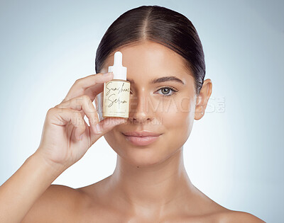 Closeup portrait beautiful woman holding face serum over eye while posing with copyspace. Young caucasian model isolated against grey studio background. Skin oil for healthy glowing skincare routine