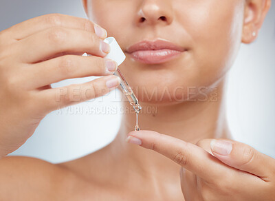 Closeup of unknown woman using dropper to put face serum on a finger. Caucasian model isolated against grey studio background getting ready to use skin oil for healthy glowing skin, skincare routine