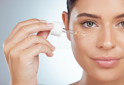 Closeup portrait of beautiful woman using dropper to apply face serum to cheek. Caucasian model isolated against grey background in a studio using skin oil for healthy glowing skin in skincare routine