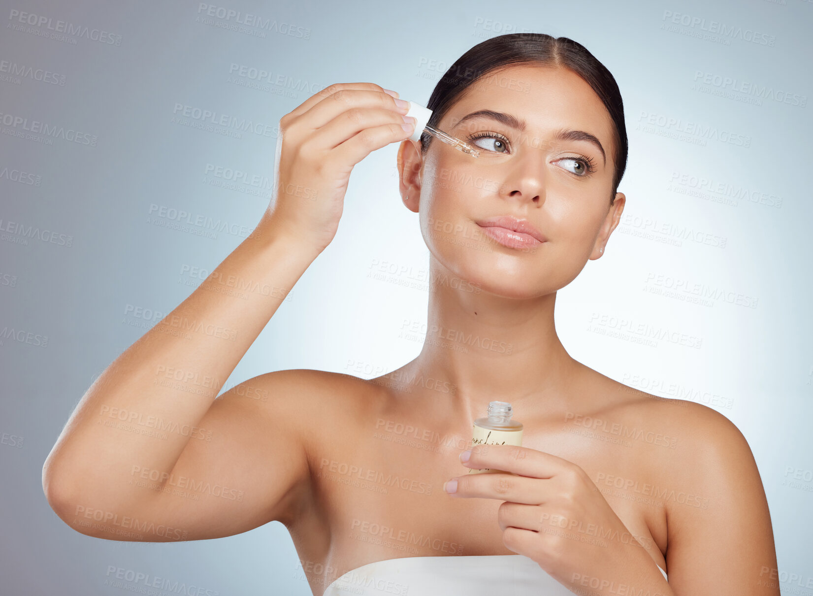 Buy stock photo Beautiful woman using dropper to apply face serum to her cheek. Caucasian model isolated against grey background in a studio and using skin oil for moisturised healthy glowing skin in skincare routine