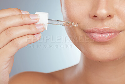 Closeup of an unknown woman using dropper to apply face serum to her lips. Caucasian model isolated against a grey background in a studio using skin oil for healthy glowing skin in skincare routine