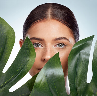 Closeup portrait of unknown woman covering her face with a green monstera plant leaf. Headshot of caucasian model posing against a grey background in a studio with smooth skin, fresh healthy skincare