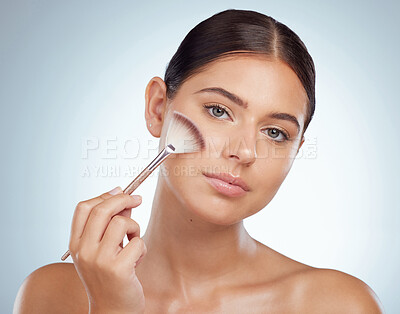 Buy stock photo Portrait of beautiful woman using cosmetic makeup brush to apply highlighter makeup while posing with copyspace. Caucasian model isolated against grey background. Getting ready after skincare routine