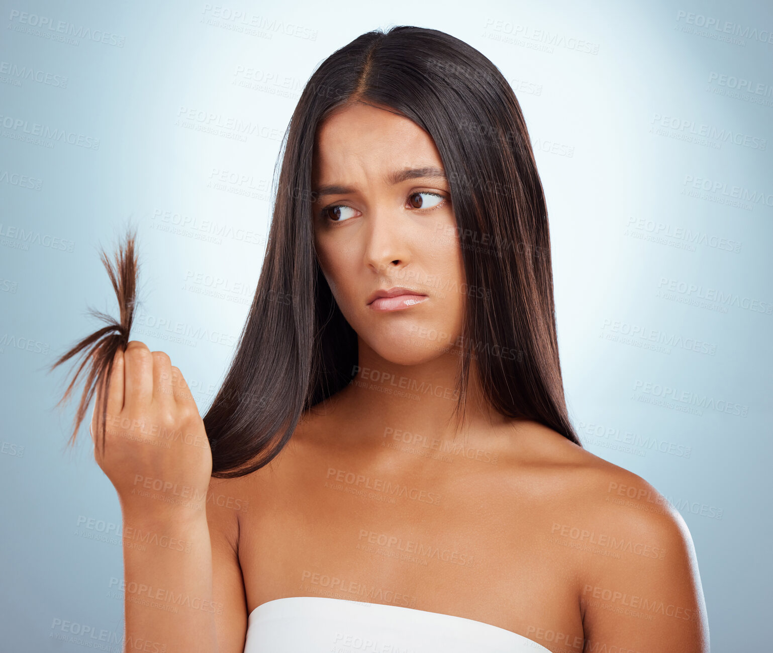 Buy stock photo A young mixed race woman looking unhappy with her unhealthy hair against a grey background. Hispanic female expressing dissatisfaction at her split ends