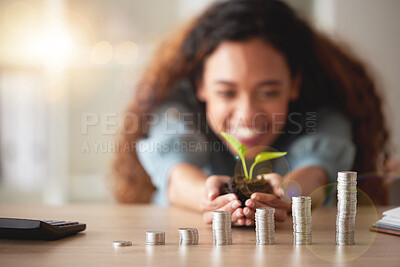 Young happy hispanic woman holding a plant growing out of soil in her hands with money coins on different levels on a table. Symbolises money growing, investment and banking