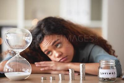 Young african american woman staring at an hour glass while looking bored at home. Mixed race person counting down while financial planning in her living room. Waiting for her investments and savings