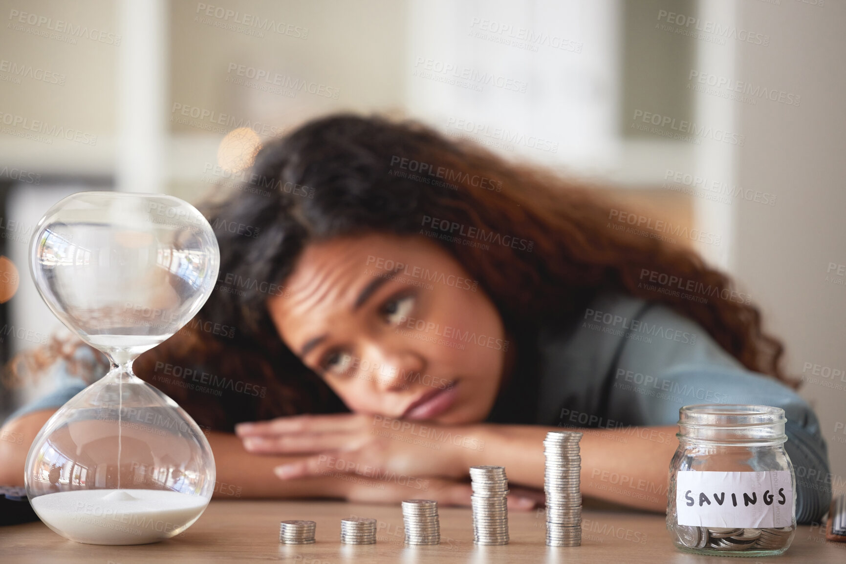 Buy stock photo Young african american woman staring at an hour glass while looking bored at home. Mixed race person counting down while financial planning in her living room. Waiting for her investments and savings