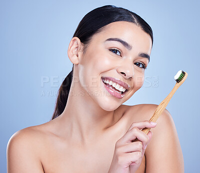Studio portrait of a smiling mixed race young woman with glowing skin posing against blue copyspace background while brushing her teeth for fresh breath. Hispanic model using toothpaste to prevent a cavity