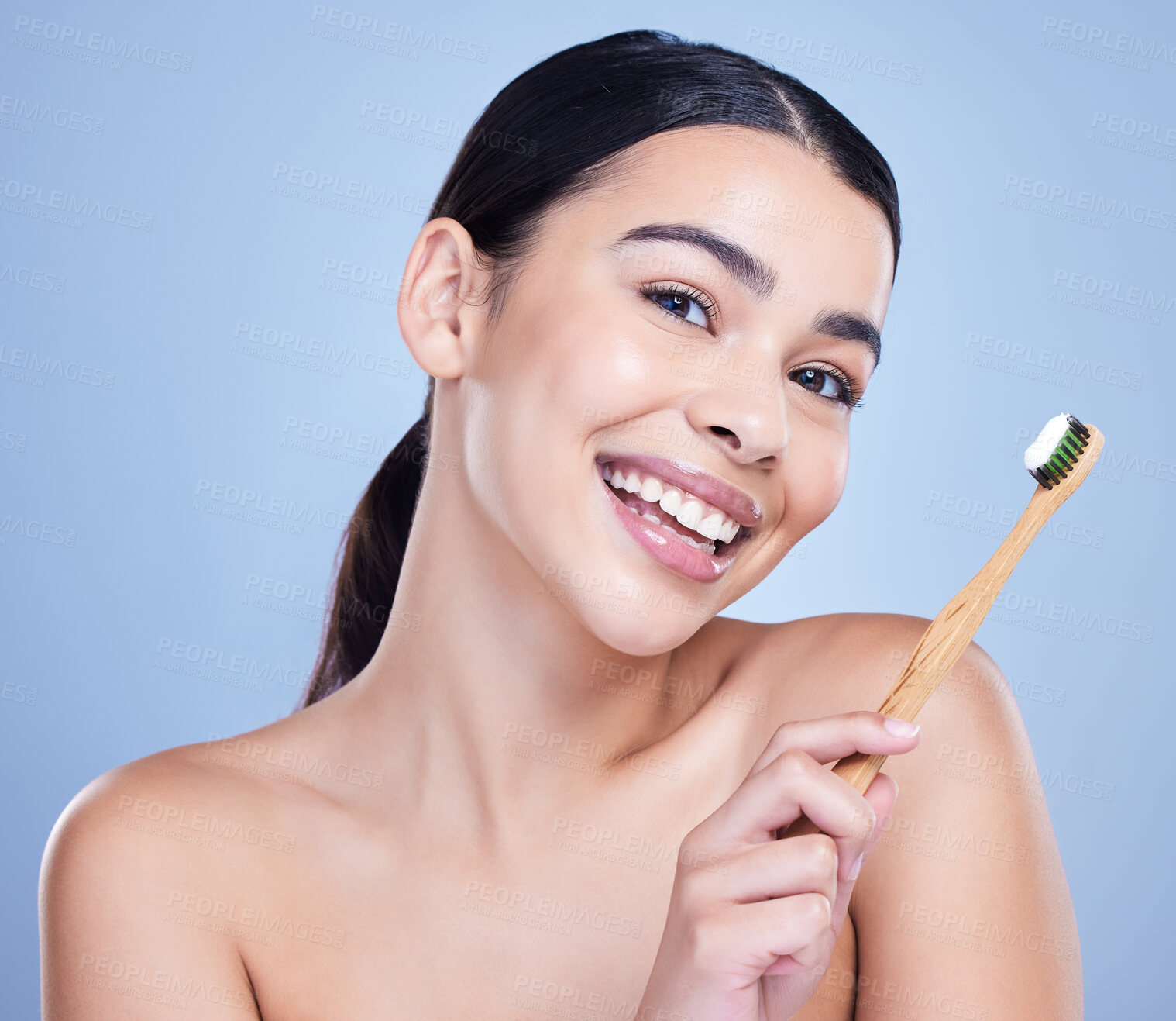 Buy stock photo Studio portrait of a smiling mixed race young woman with glowing skin posing against blue copyspace background while brushing her teeth for fresh breath. Hispanic model using toothpaste to prevent a cavity