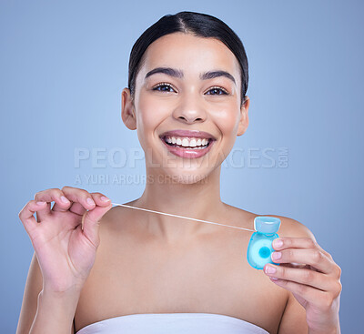 Buy stock photo Studio portrait of a smiling mixed race young woman with glowing skin posing against blue copyspace background while flossing her teeth for fresh breath. Hispanic model using floss to prevent a cavity