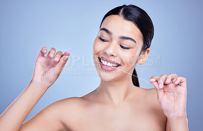 A happy smiling mixed race young woman with glowing skin posing against blue copyspace background while flossing her teeth for fresh breath. Hispanic model using floss to prevent a cavity