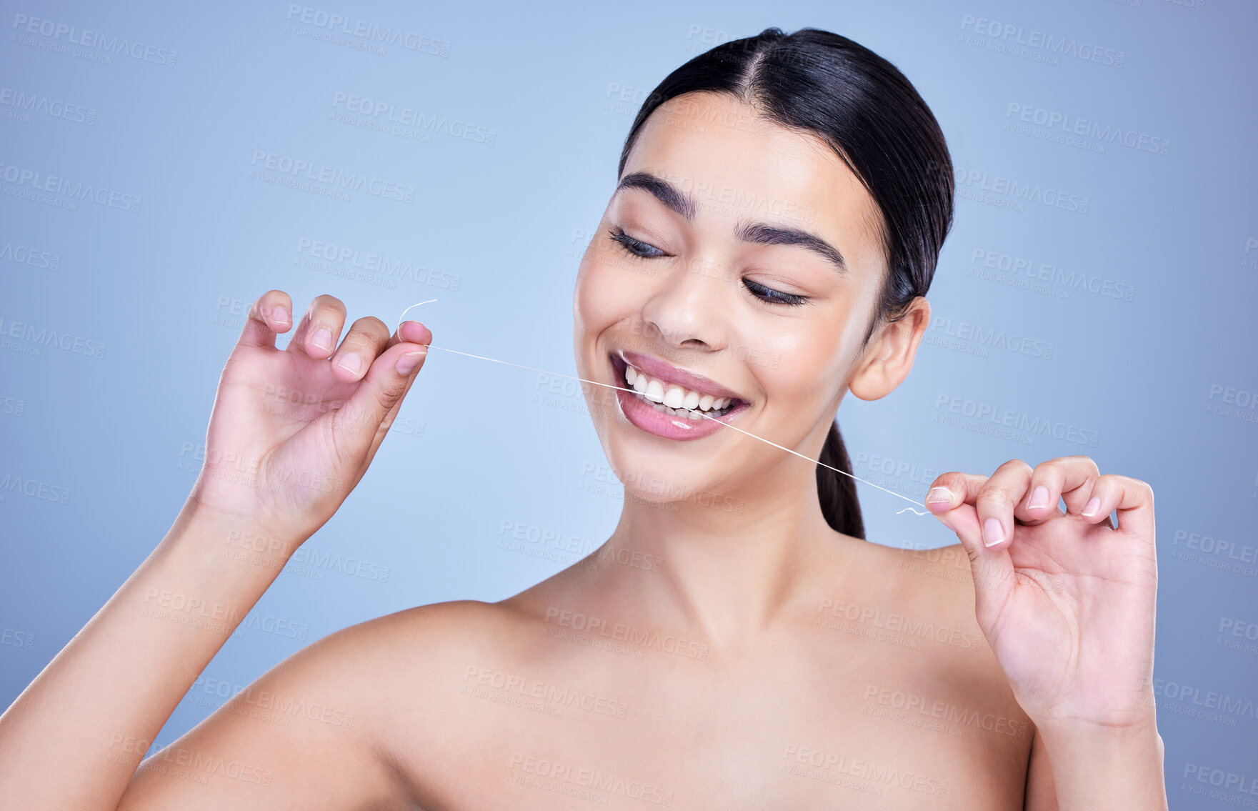 Buy stock photo A happy smiling mixed race young woman with glowing skin posing against blue copyspace background while flossing her teeth for fresh breath. Hispanic model using floss to prevent a cavity