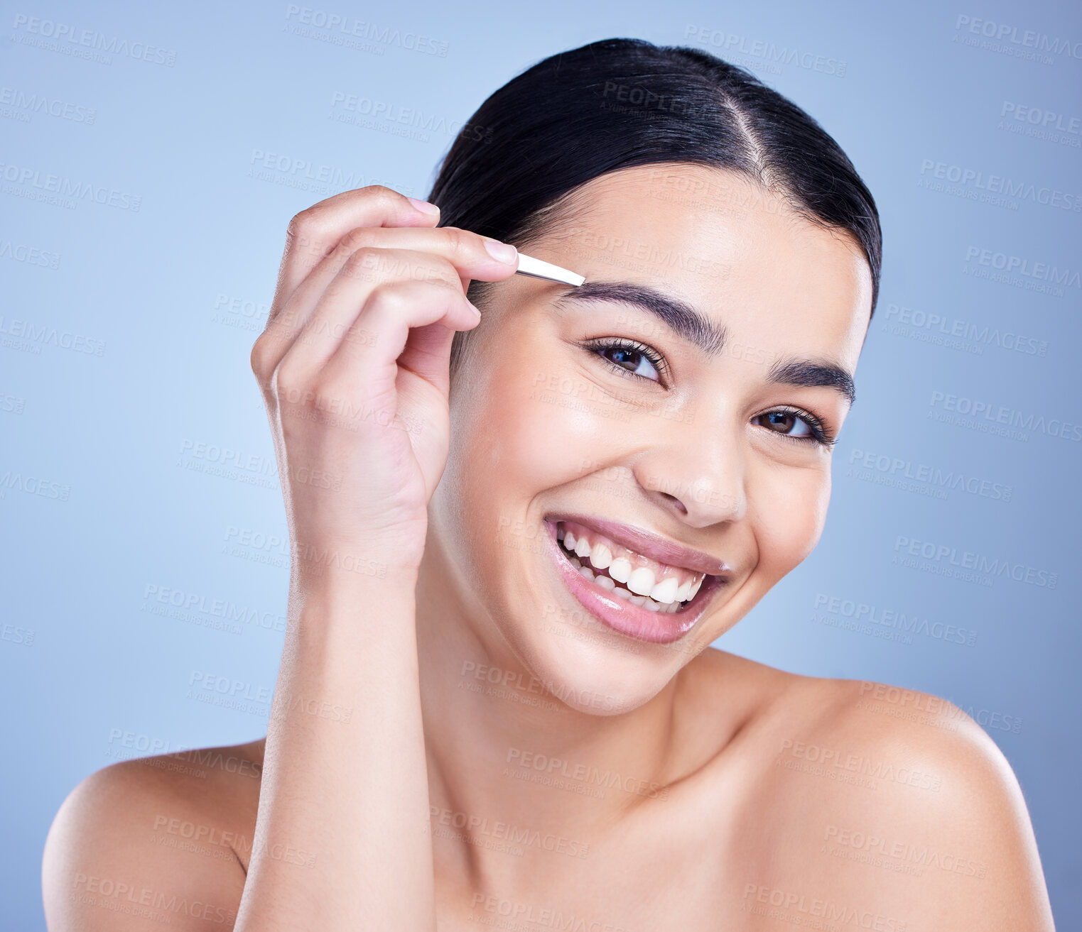 Buy stock photo Studio portrait of a smiling mixed race young woman with glowing skin posing against blue copyspace background while tweezing her eyebrows. Hispanic model using a tweezer for hair removal