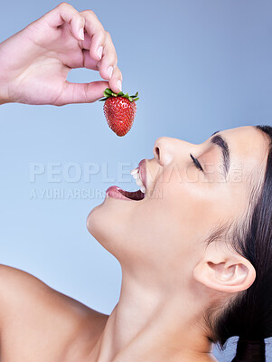Buy stock photo A happy smiling mixed race woman eating a strawberry. Hispanic model promoting the skin benefits of a healthy diet against a blue copyspace background