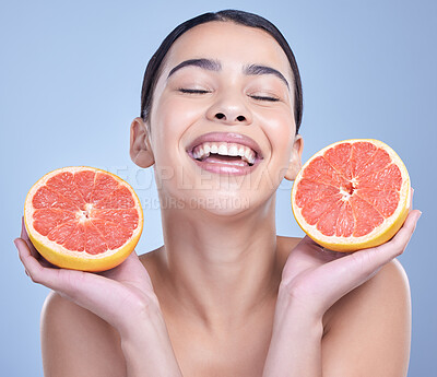 A happy mixed race woman holding a grapefruit. Hispanic model promoting the skin benefits of citrus diet against a blue copyspace background