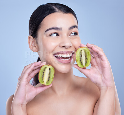 A happy smiling mixed race woman holding a kiwi fruit. Hispanic model promoting the skin benefits of a healthy diet against a blue copyspace background