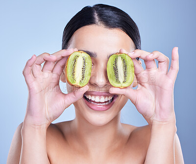 A happy smiling mixed race woman holding a kiwi fruit. Hispanic model promoting the skin benefits of a healthy diet against a blue copyspace background