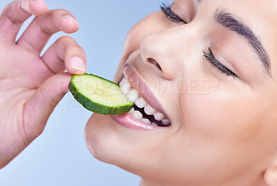 Buy stock photo A beautiful mixed race woman holding cucumber slice. Hispanic model promoting the skin benefits of a healthy diet against a blue copyspace background