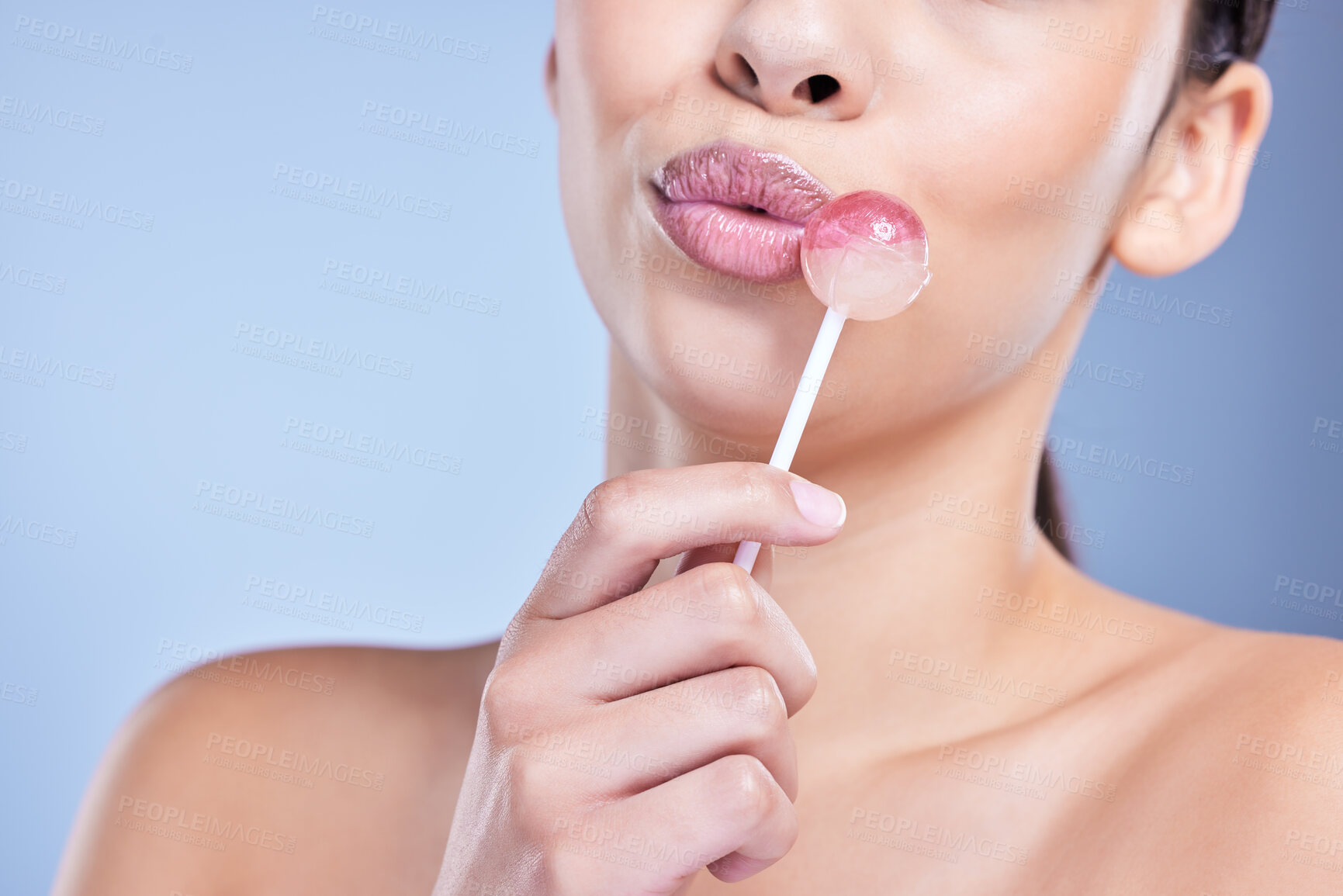 Buy stock photo Closeup of a a beautiful mixed race model playfully licking a lollipop in studio against a blue background copyspace