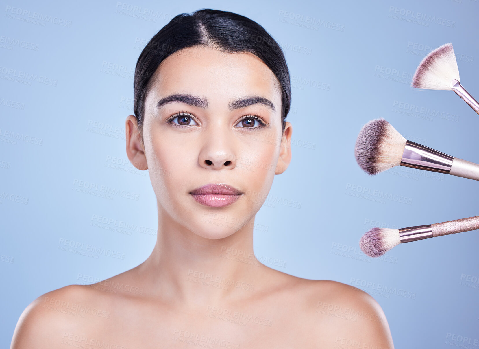 Buy stock photo Studio Portrait of a beautiful mixed race woman posing with a collection of makeup brushes during pamper routine. Hispanic model with cosmetic tools standing against a blue copyspace background