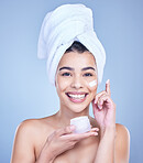 Studio Portrait of a beautiful smiling mixed race woman applying cream to her face. Hispanic model with glowing skin holding moisturiser against a blue copyspace background