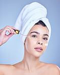 Studio Portrait of a beautiful mixed race woman applying a soothing face serum to her radiant smooth face while posing against a blue background. Hispanic woman with flawless skin using essential oil