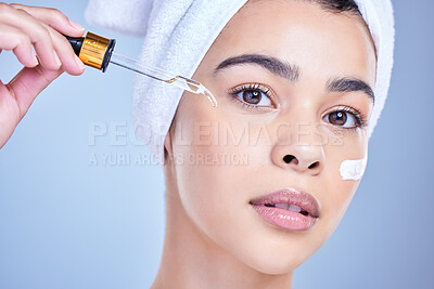 Buy stock photo Studio Portrait of a beautiful mixed race woman applying a soothing face serum to her radiant smooth face while posing against a blue background. Hispanic woman with flawless skin using essential oil