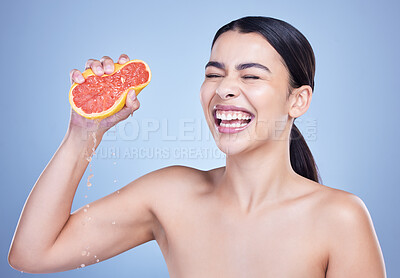 A happy mixed race woman holding a grapefruit. Hispanic model promoting the skin benefits of citrus diet against a blue copyspace background