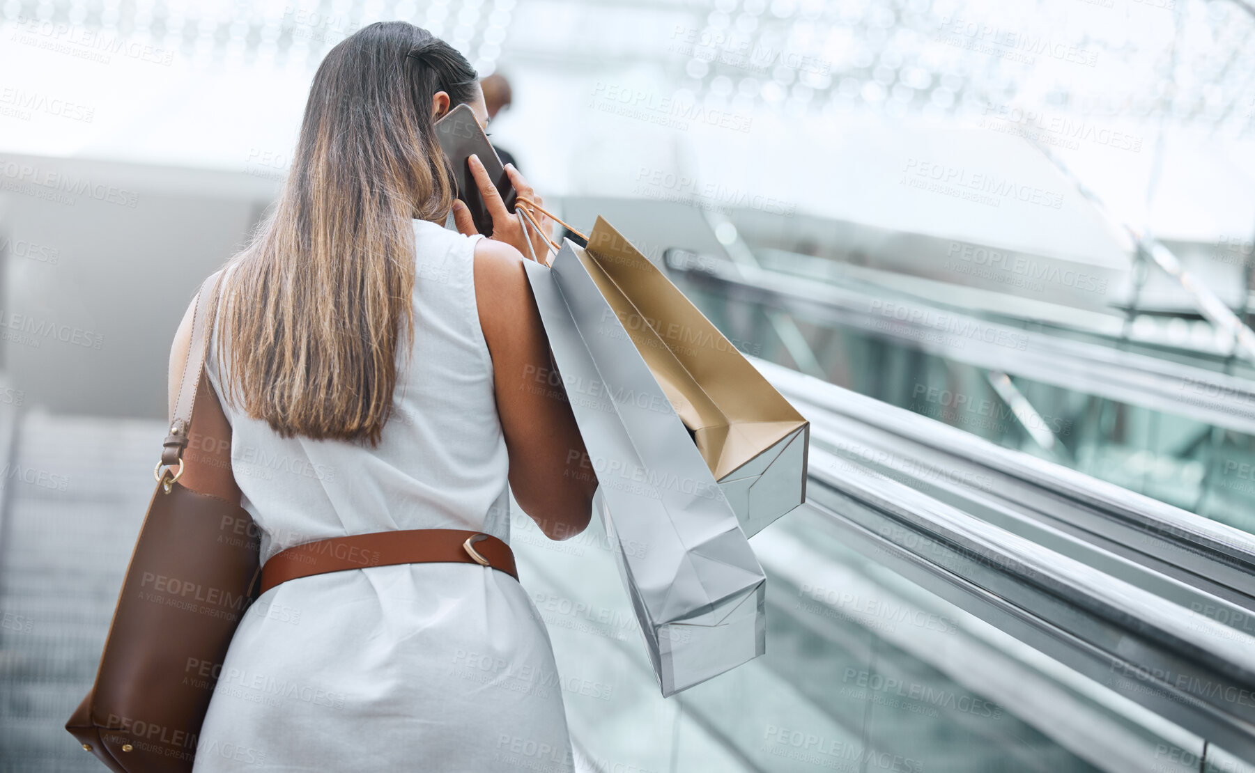 Buy stock photo Rear view of a woman talking on her cellphone while out on a shopping spree. Female having retail therapy while staying connected with her smartphone. Calling to find a sale and discount. Telling friends about sale at mall or calling bank to increase spending limit