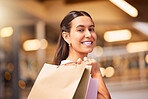 Portrait of a young mixed race woman carrying shopping  bags over her shoulder in a mall. One hispanic female only enjoying retail therapy. Shopaholic holding bags smiling and looking happy while walking in a shopping mall