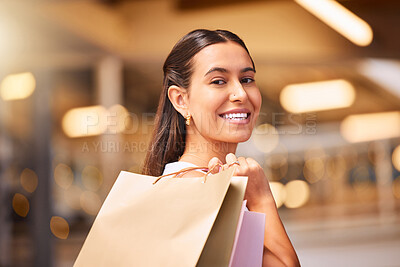 Portrait of a young mixed race woman carrying shopping bags over her shoulder in a mall. One hispanic female only enjoying retail therapy. Shopaholic holding bags smiling and looking happy while walking in a shopping mall