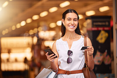 Portrait of young mixed race woman using a cell phone and bank card while carrying shopping bags in a mall. Young woman purchasing items online with her smartphone and credit card in a shopping mall. Woman using banking app or checking for discount while