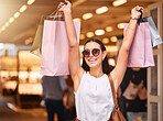 Portrait of a young mixed race woman wearing sunglasses and holding up showing bags during a shopping spree in a mall. Hispanic female enjoying retail therapy while looking excited. Shopaholic holding bags smiling and looking happy