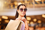Stylish young woman wearing glasses and holding shopping bags over her shoulder against a blurred background. Woman relaxing and enjoying shopping on the weekend