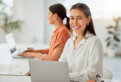 Portrait of one confident young hispanic business woman working on a laptop in an office with her colleague in the background. Happy entrepreneur browsing the internet while planning ideas at her desk in a creative startup agency