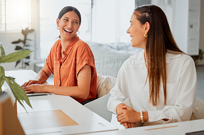 Cheerful young hispanic business woman working on a laptop while talking to a colleague in an office. Two happy coworkers working together in a creative startup agency