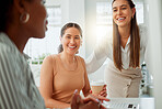 Group of confident smiling young business women brainstorming together in an office. Cheerful hispanic woman drinking coffee while listening to her colleague discussing plans
