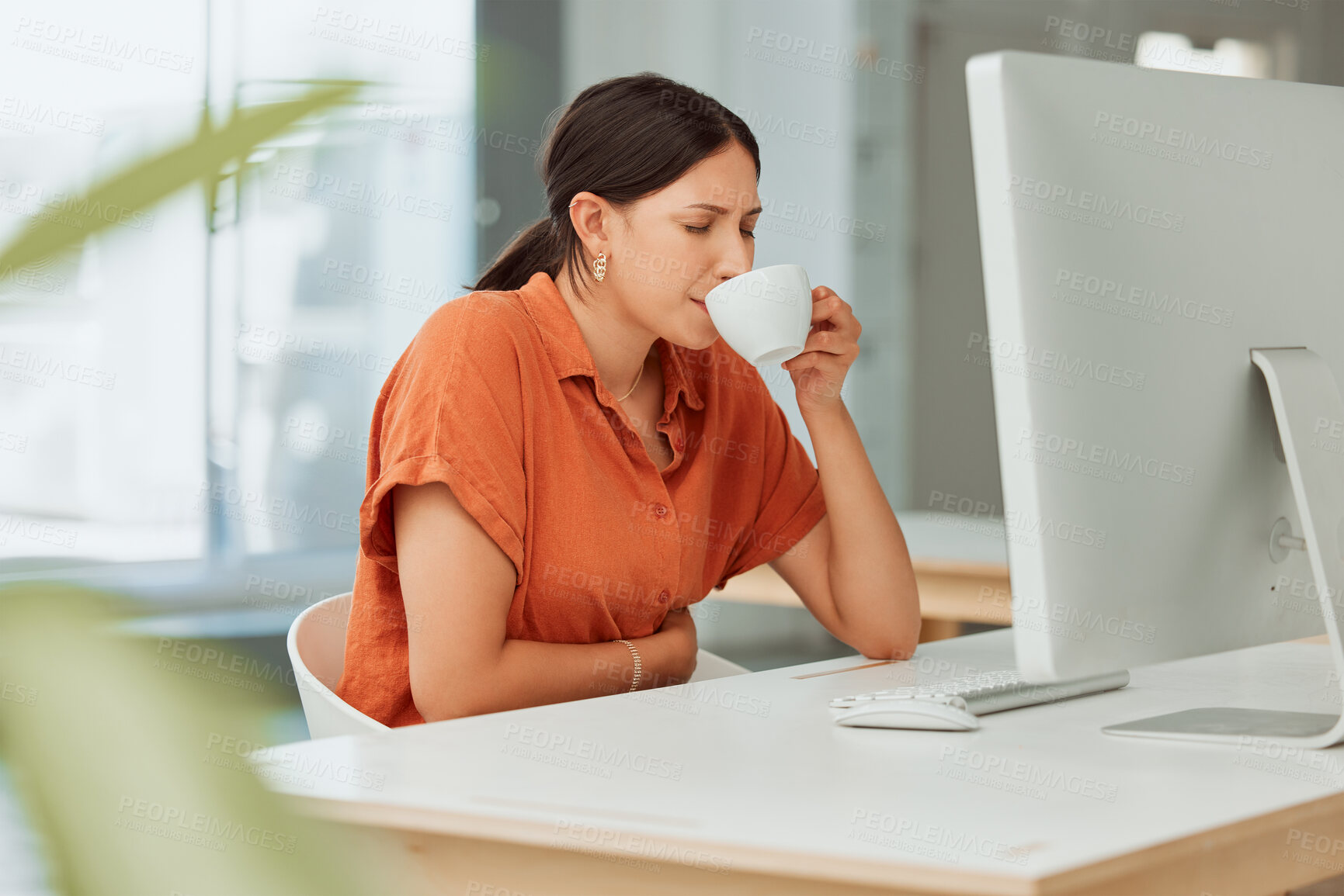 Buy stock photo One hispanic business woman drinking warm tea as a remedy for sore tummy while feeling ill with menstrual stomach cramps in an office. Sick employee on period taking medicine for bloated and uncomfortable digestive pain caused by stress and anxiety