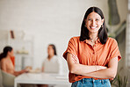 Portrait of one confident young hispanic business woman standing with arms crossed in an office with her colleagues in the background. Ambitious entrepreneur and determined leader ready for success in a creative startup agency