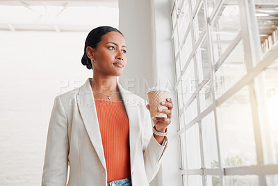 Young mixed race businesswoman drinking a coffee alone in an office at work. Confident hispanic businessperson looking out of a window drinking a coffee standing at work