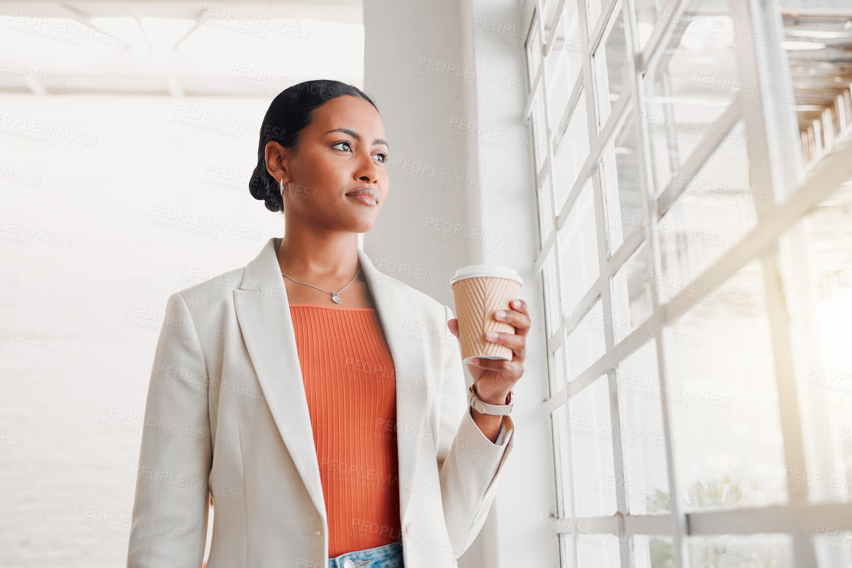 Buy stock photo Young mixed race businesswoman drinking a coffee alone in an office at work. Confident hispanic businessperson looking out of a window drinking a coffee standing at work