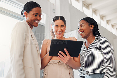 Buy stock photo Group of cheerful businesswomen talking and working on a digital tablet together at work. Joyful businesspeople talking and planning while standing in an office